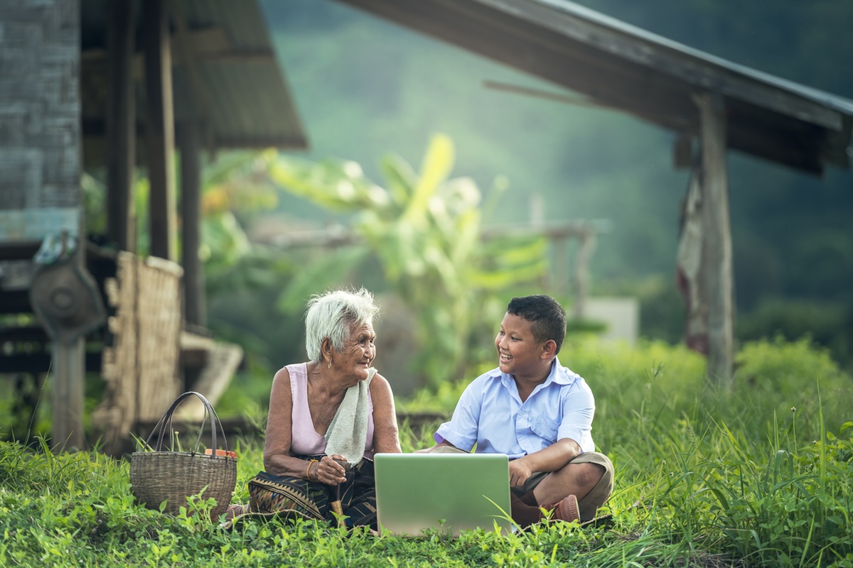 Un niño asiático con su abuela viendo un dispositivo portátil sentados en el pasto